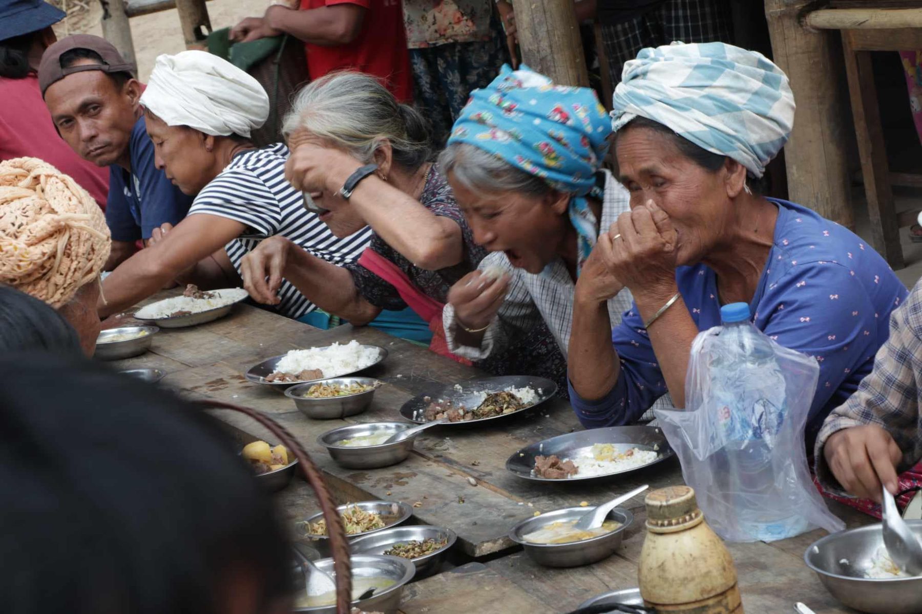 Elderly people in head wraps eat together at a long table.