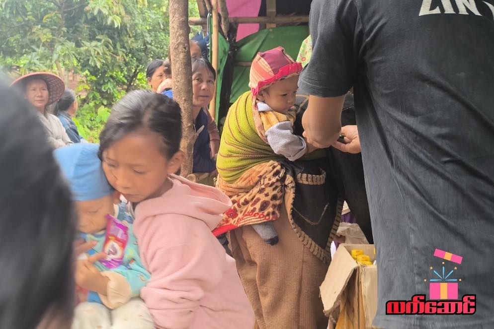 A girl in a pink jacket and a woman carrying a baby receive supplies.